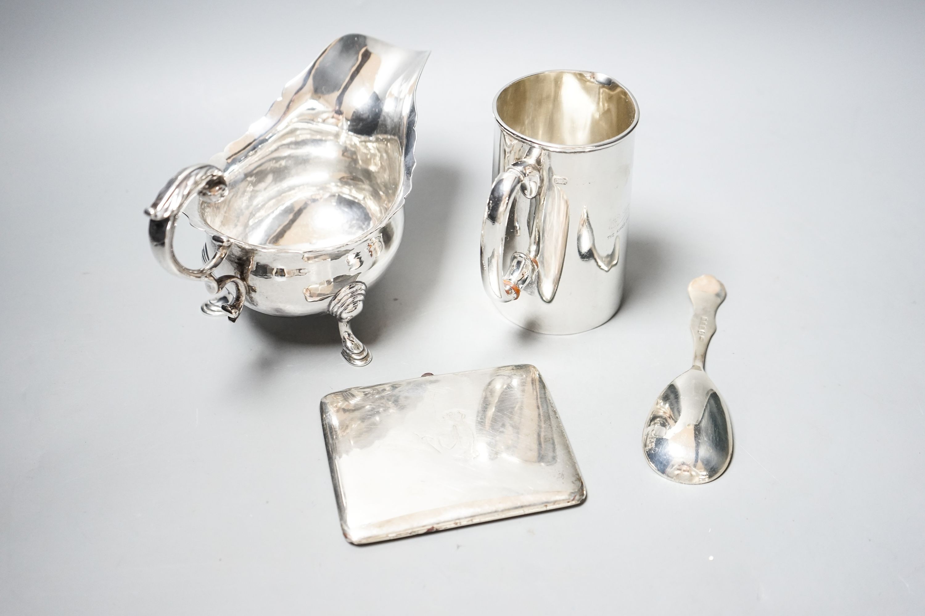 A George V silver sauceboat, a silver jug with military related inscription, a silver cigarette case and silver spoon